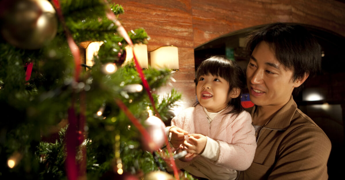 An adult and child look at a lit Christmas Tree. Interior, evening/night.