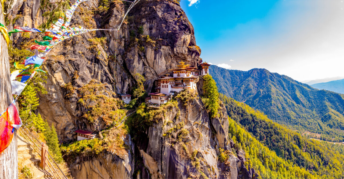 Wide shot, the taktsang, Bhutan. A multi-level, white, red, and gold building built against the side of a mountain. Exterior, day.