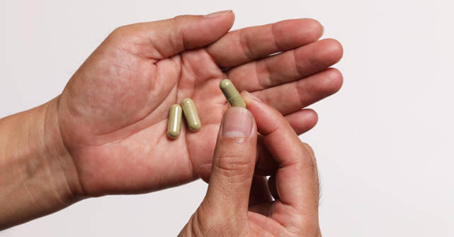 Hands holding tan-colored supplement capsules